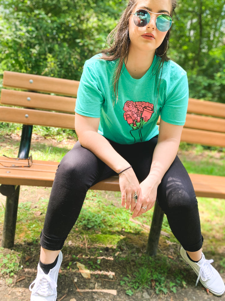 Woman sits on a bench wearing the green bouquet of audio cables tee
