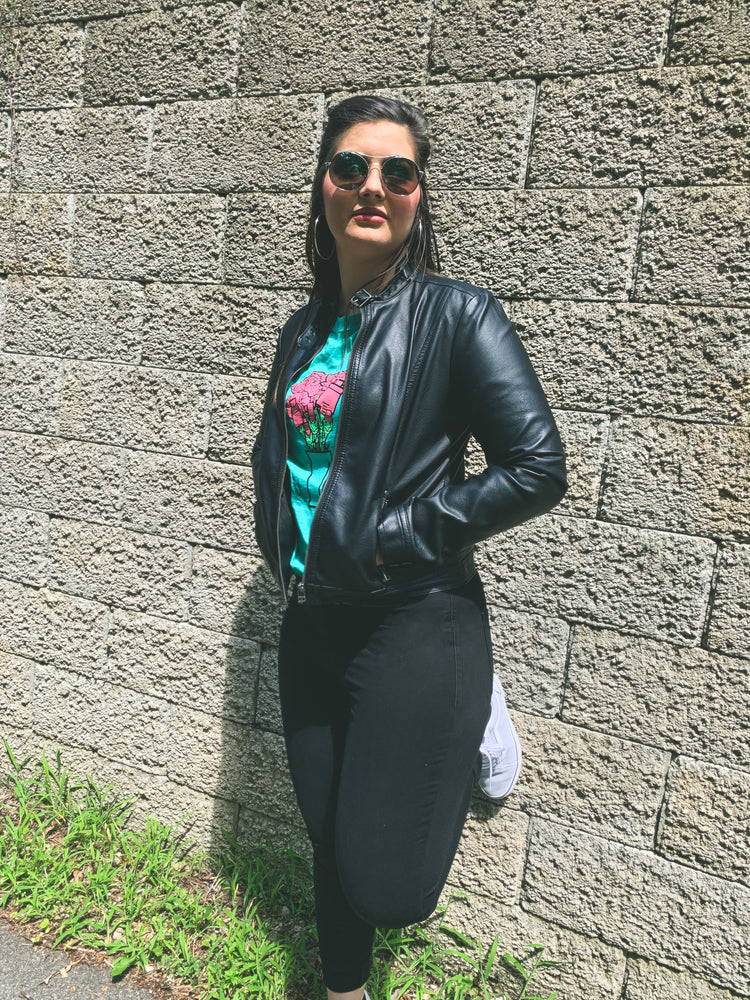 Woman stands against a wall wearing the green bouquet of audio cables tee